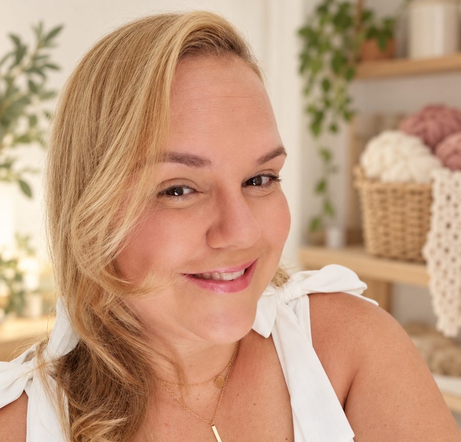 Carol, a artesã, sorrindo em seu ateliê, com cestos de novelos ao fundo